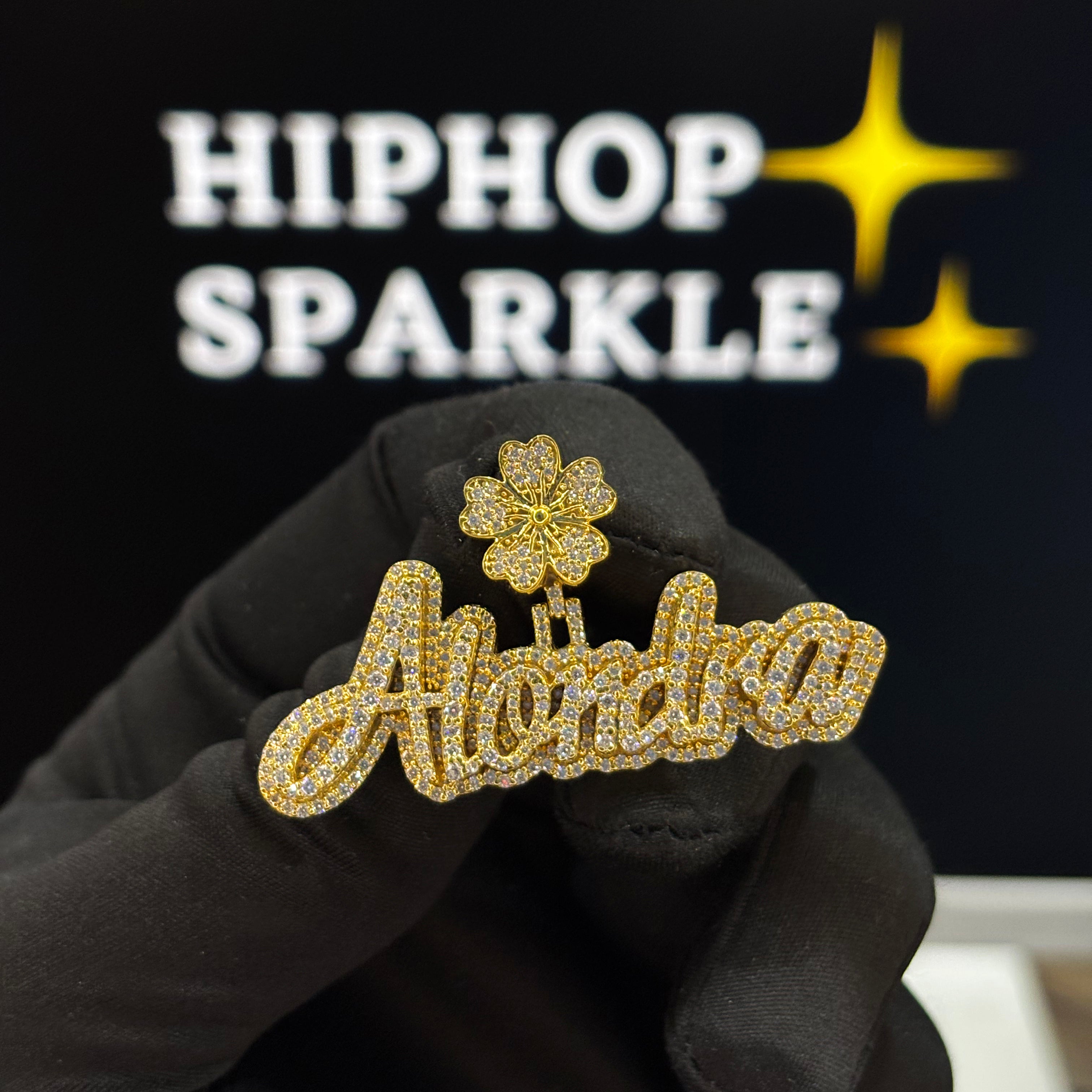 Gold floral brooch with 'Alondra' text held by a gloved hand against a black background with 'HIPHOP SPARKLE' text.